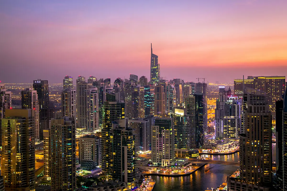 City skyline at sunset, lights reflecting on the marina.