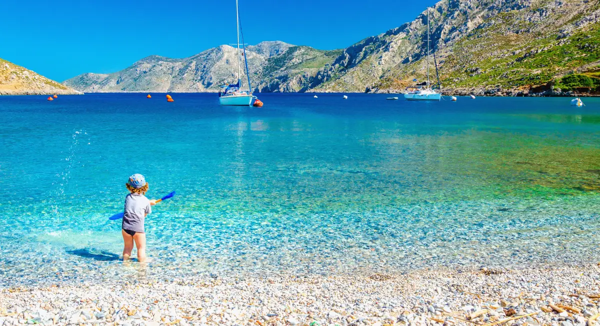 A mother taking a picture of their child playing happily by the sea in Mykonos, in Greece, a family-friendly, warm location.